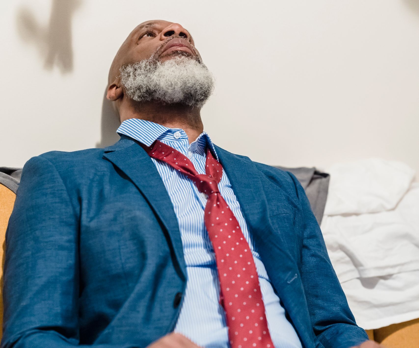 Elderly man in a suit looking upwards, wearing a red tie, appears thoughtful.