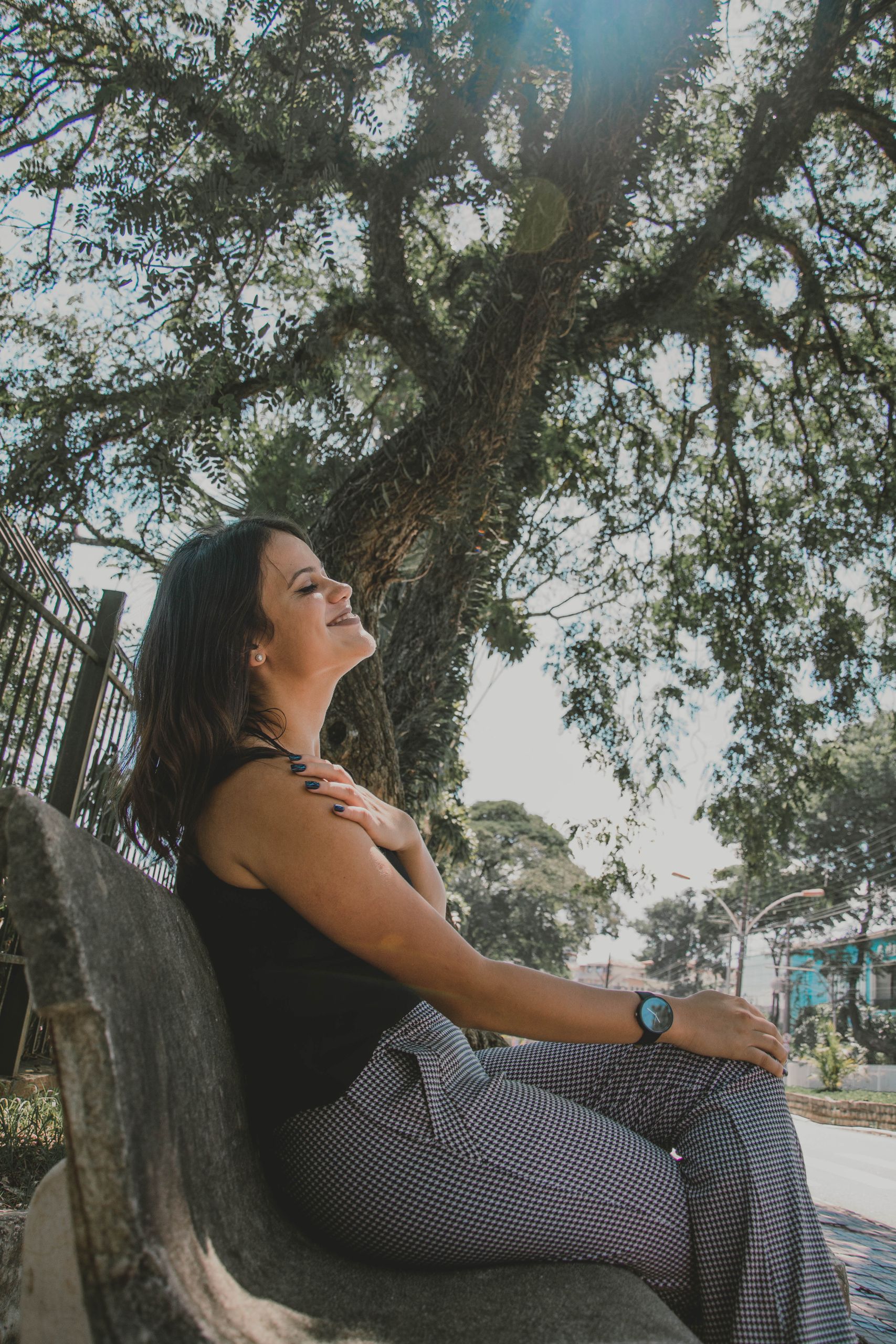 A woman sitting on a bench, enjoying a sunny day under a tree. Perfect outdoor relaxation.