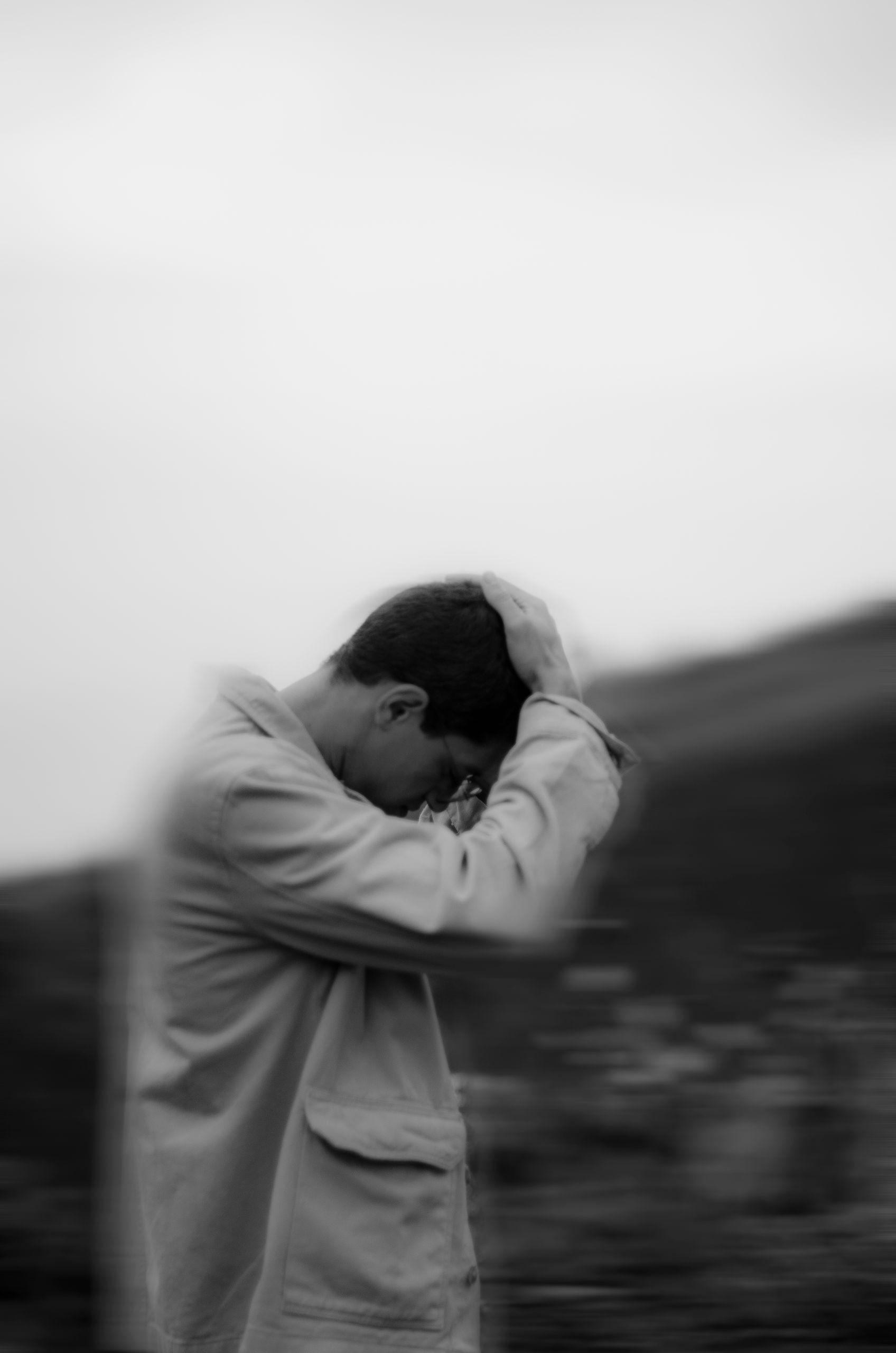 Black and white portrait of a person in a reflective pose outdoors, conveying emotion.